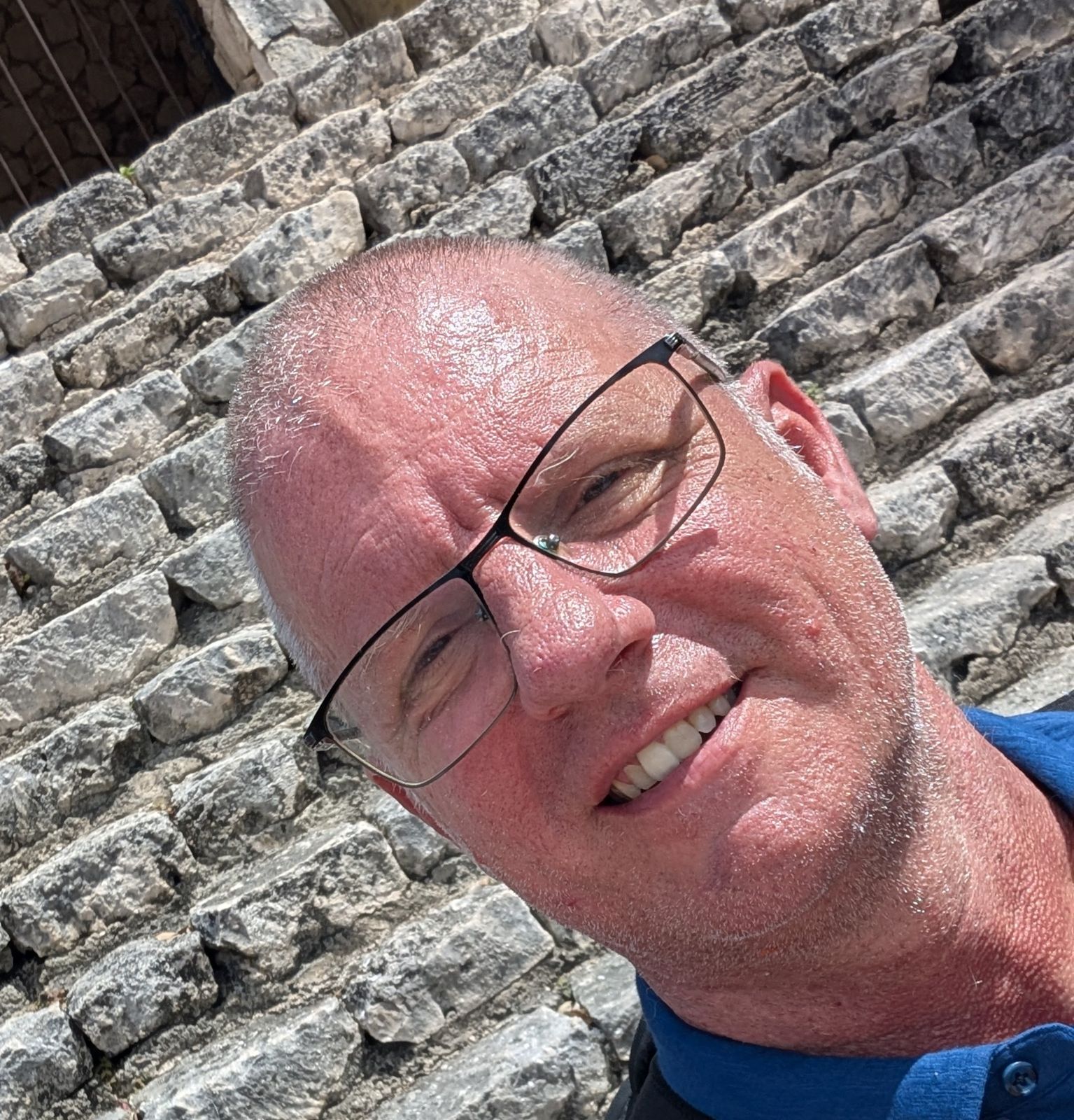 Jonathan smiling in glasses against a stone wall